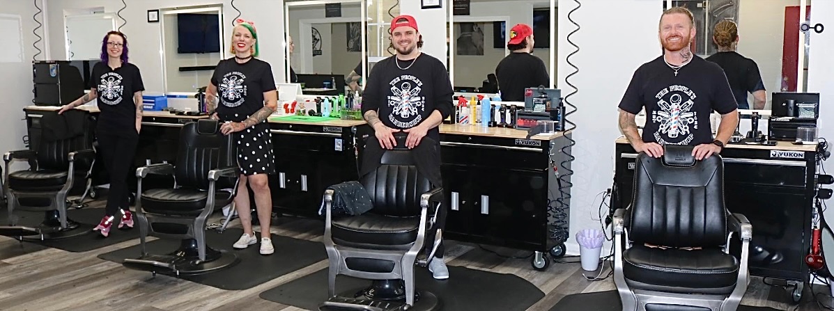 The barbers of The People’s Barbershop standing behind their chairs in matching shop T-shirts